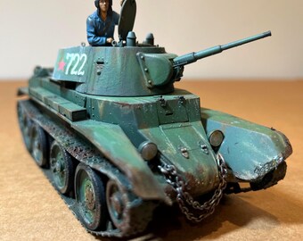 May include: A detailed model of a green military tank with a long gun barrel. The tank has visible rust and wear, with the number "722" in red on the side. A small figure of a soldier in a blue uniform is in the open hatch.