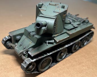 May include: A detailed model of a military tank in shades of green and brown. The tank features a rotating turret with a gun barrel, tracks, and wheels. The model appears to be weathered, with visible details.