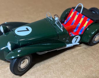 May include: A dark green vintage race car model with the number 1 on the hood and side. The interior features red seats and blue and yellow seatbelts. The car has a black spare tire and a silver roll bar.