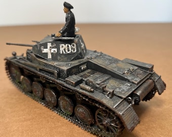 May include: A detailed model of a military tank, painted in shades of gray and brown, with visible wear and tear. The turret displays a white cross and the number "R03". A miniature figure in a black uniform sits atop the tank.