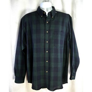 May include: A long-sleeved button-down shirt in a green and navy plaid pattern. The shirt has a button-down collar, a chest pocket, and gold-colored buttons. The shirt is displayed on a white mannequin.