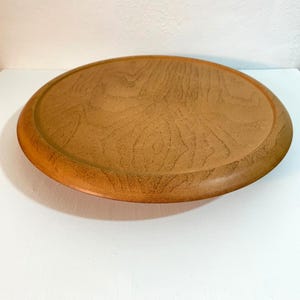 May include: A round, wooden serving tray with a raised edge. The tray has a natural wood grain pattern and a warm, brown color. The tray is approximately 12 inches in diameter.