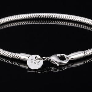 Könnte beinhalten: Ein silberfarbenes Armband mit Schlangenketten-Design. Das Armband hat einen Karabinerverschluss und ein kleines, rundes Etikett mit der Aufschrift "925". Das Armband wird auf einer reflektierenden schwarzen Oberfläche präsentiert.