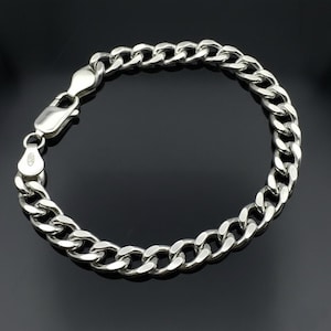 Peut inclure: Un bracelet chaîne gourmette argenté avec un fermoir mousqueton. Le bracelet est en métal poli et présente une série de maillons arrondis interconnectés. Le fermoir est solidement fixé, et le bracelet est présenté sur un fond sombre.