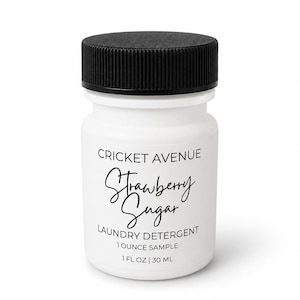 May include: A small white plastic bottle with a black screw-top lid containing laundry detergent. The label reads CRICKET AVENUE, Strawberry Sugar, LAUNDRY DETERGENT, 1 OUNCE SAMPLE, and 1 FL OZ | 30 ML in black text on the white surface.