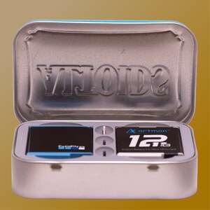 May include: A silver metal tin with a blue rim, containing two black memory cards and a small compartment. One card has the GoPro logo and blue accents. The other card has the text "artman" and "12T64". The tin's lid has the embossed word "VITOID2".