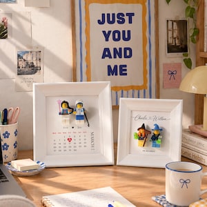 May include: Two white framed displays featuring custom LEGO minifigures. The left frame shows a March calendar with the names Eva and Jay. The right frame displays the names Charlie and Willson with the date 19.04.2025 and two witch-themed minifigures.