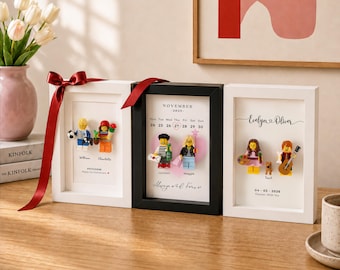 Puede incluir: Tres marcos de caja rectangulares que contienen minifiguras personalizadas y texto impreso. El marco izquierdo es blanco con una cinta roja, el central es negro con un calendario de noviembre de 2025 y el derecho es blanco con los nombres Evelyn y Oliver.