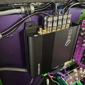 May include: A black audio amplifier with multiple input and output connectors, mounted vertically against a purple surface. The text "Flush Mounted verical" is visible at the top. Cables and wiring are connected to the amplifier.