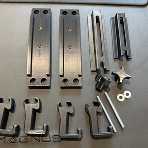 May include: An assortment of black metal hardware components, including brackets, rails, knobs, and screws, arranged on a dark surface. The pieces appear to be for a mounting or support system.