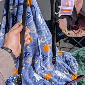 May include: Black leather handbag strap with silver-coloured fastenings. The strap is displayed against a blue Halloween-themed blanket with white ghosts, orange pumpkins, and witch hats.