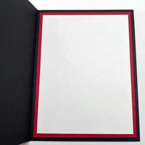 Pode incluir: Um cart&atilde;o de felicita&ccedil;&otilde;es aberto com interior branco, borda vermelha e moldura preta. O cart&atilde;o est&aacute; aberto, revelando o espa&ccedil;o em branco para uma mensagem. O design do cart&atilde;o &eacute; simples e elegante.