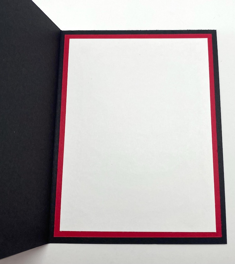 Pode incluir: Um cart&atilde;o de felicita&ccedil;&otilde;es aberto com interior branco, borda vermelha e moldura preta. O cart&atilde;o est&aacute; aberto, revelando o espa&ccedil;o em branco para uma mensagem. O design do cart&atilde;o &eacute; simples e elegante.