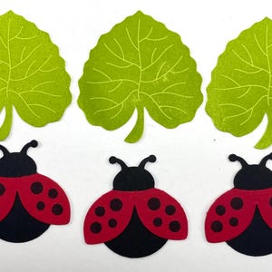 Pode incluir: Tr&ecirc;s recortes de folhas verdes e tr&ecirc;s recortes de joaninhas. As joaninhas t&ecirc;m asas vermelhas com pintas pretas e corpos pretos. As folhas s&atilde;o verde claro com padr&otilde;es de veias detalhados.