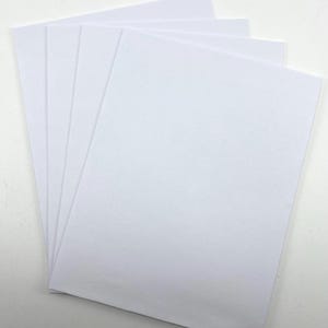 Pode incluir: Uma pilha de folhas de papel brancas e retangulares, ligeiramente em leque. O papel &eacute; branco brilhante e parece liso. As folhas est&atilde;o empilhadas umas sobre as outras, com as bordas vis&iacute;veis.
