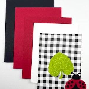 Pode incluir: Um cart&atilde;o com um padr&atilde;o xadrez preto e branco, uma folha verde e uma joaninha. O cart&atilde;o &eacute; acompanhado por cartolina preta, vermelha e branca. A joaninha &eacute; vermelha com pintas pretas e cabe&ccedil;a preta.