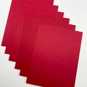 Pode incluir: Uma pilha de folhas de papel vermelho, dispostas em um padr&atilde;o ligeiramente em leque. O papel tem uma textura suave e uma cor vermelha s&oacute;lida e vibrante. As folhas s&atilde;o retangulares e parecem ser de tamanho A4.