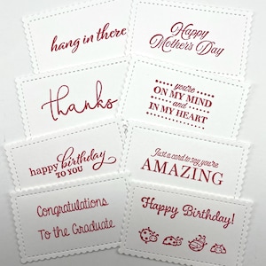 Pode incluir: Uma cole&ccedil;&atilde;o de cart&otilde;es retangulares brancos com bordas onduladas e texto vermelho. Os cart&otilde;es apresentam v&aacute;rias mensagens, incluindo "Feliz Dia das M&atilde;es", "Obrigado" e "Feliz Anivers&aacute;rio". Alguns cart&otilde;es t&ecirc;m ilustra&ccedil;&otilde;es de joaninhas.