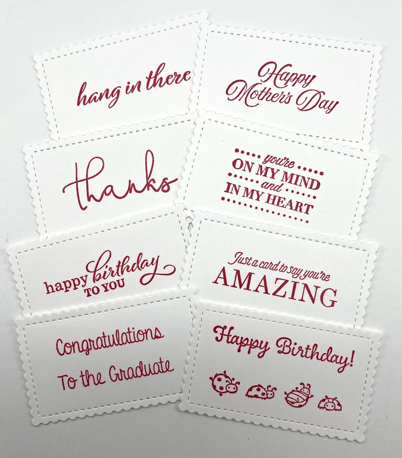 Pode incluir: Uma cole&ccedil;&atilde;o de cart&otilde;es retangulares brancos com bordas onduladas e texto vermelho. Os cart&otilde;es apresentam v&aacute;rias mensagens, incluindo "Feliz Dia das M&atilde;es", "Obrigado" e "Feliz Anivers&aacute;rio". Alguns cart&otilde;es t&ecirc;m ilustra&ccedil;&otilde;es de joaninhas.