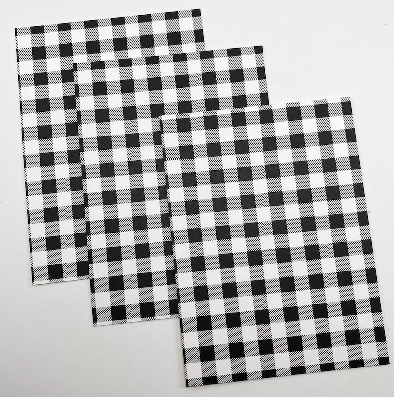 Pode incluir: Tr&ecirc;s folhas de papel retangulares com um padr&atilde;o xadrez preto e branco. O padr&atilde;o consiste em quadrados uniformemente espa&ccedil;ados, criando um design xadrez cl&aacute;ssico. As folhas s&atilde;o dispostas de forma ligeiramente sobreposta, mostrando a repeti&ccedil;&atilde;o do padr&atilde;o.