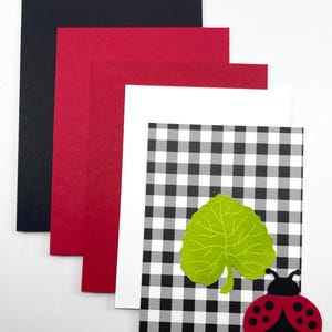 Pode incluir: Um cart&atilde;o com um padr&atilde;o xadrez preto e branco, uma folha verde e uma joaninha. O cart&atilde;o &eacute; acompanhado por cartolina preta, vermelha e branca. A joaninha &eacute; vermelha com pintas pretas e uma cabe&ccedil;a preta.