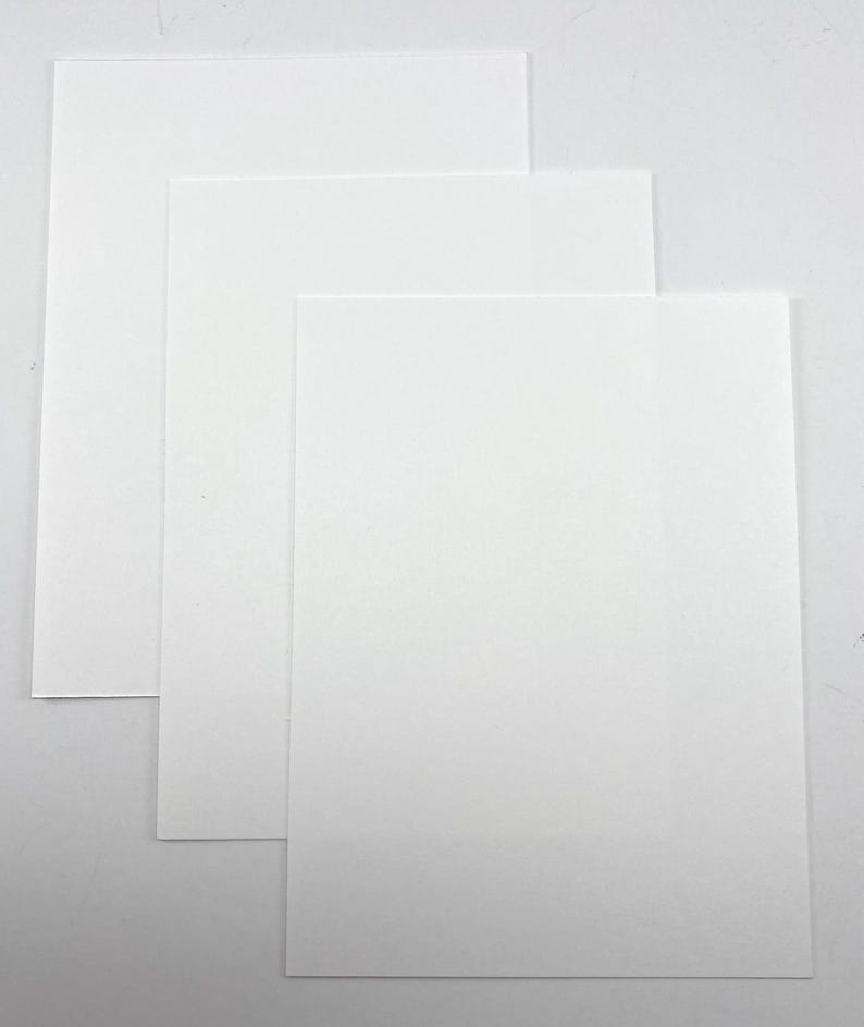 Pode incluir: Tr&ecirc;s folhas de papel retangulares brancas, ligeiramente sobrepostas. O papel tem um acabamento liso e fosco e est&aacute; disposto sobre um fundo branco liso. As folhas variam ligeiramente de tamanho, criando um efeito em camadas.
