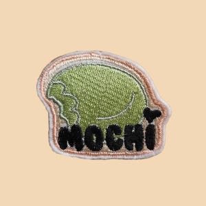 May include: A green mochi embroidered patch with pink and white stitching around the edges. The word "MOCHI" is embroidered in black.