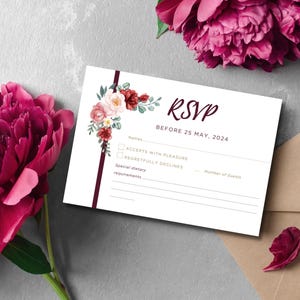 Può includere: Biglietto RSVP bianco con decorazioni floreali, con testo: "RSVP BEFORE 25 MAY, 2024." Include spazi per nomi, accettazione, rifiuto, esigenze dietetiche e numero di invitati. Circondato da peonie bordeaux e una busta di carta kraft.