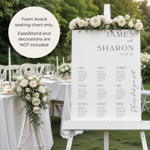 May include: A white foam board seating chart, featuring the names "James and Sharon" and the date "15.08.28". The chart is adorned with white flowers and lists guest names. The easel and decorations are not included.