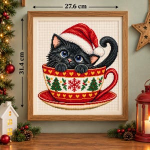 Puede incluir: Un cuadro de punto de cruz enmarcado que muestra un gatito negro con un gorro de Papá Noel rojo y blanco, sentado dentro de una taza roja decorada con árboles de Navidad verdes, copos rojos y corazones amarillos, de 27,6 cm por 31,4 cm.