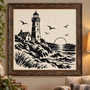 Puede incluir: Un bordado en punto de cruz enmarcado que presenta una escena costera en blanco y negro. El diseño muestra un faro, una casa pequeña, acantilados rocosos, hierba alta y pájaros volando sobre un mar con un sol naciente en el horizonte.