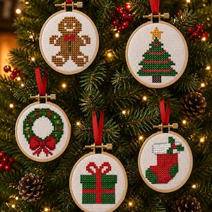 Op de afbeelding: Vijf ronde houten borduurringen met kruissteekontwerpen van een peperkoekmannetje, een kerstboom, een krans, een cadeau en een kerstsok. Elke ring hangt aan een rood lint en is voorzien van een witte stoffen achtergrond.