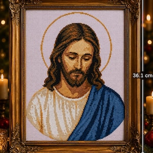 May include: A cross-stitch portrait of Jesus with long brown hair and a beard, wearing a white robe and a blue mantle, set within an ornate gold frame. The artwork measures 28.9 cm in width and 36.1 cm in height, featuring a gold halo.