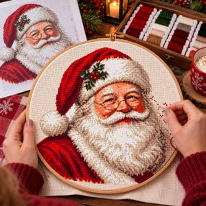 Peut inclure: Un tambour à broder rond en bois contenant un projet de point de croix représentant le Père Noël avec une barbe blanche, un bonnet rouge et un brin de houx. Le motif est réalisé sur un tissu beige, avec un guide imprimé et une boîte de fils.