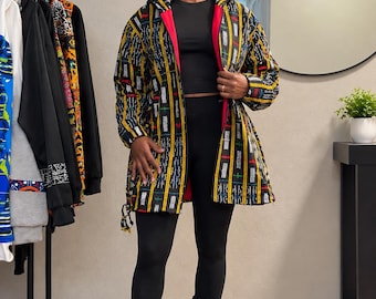 May include: A hooded jacket featuring a black base with vertical yellow, white, and red patterned stripes. The jacket has a bright red interior lining, long sleeves, and a drawstring hem. It is worn over a black crop top and black leggings.