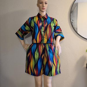 May include: A two-piece outfit on a mannequin. The set includes a collared, short-sleeved shirt and matching shorts. The fabric features a vibrant pattern of colourful, stylised leaves in shades of blue, red, yellow, and green.