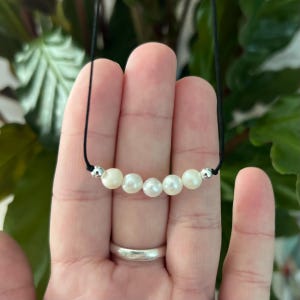 May include: A simple necklace with a black cord and five white pearls. The pearls are evenly spaced and the cord is tied with a knot at the back.