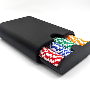 Op de afbeelding: Een matzwarte rechthoekige schuifdoos met drie rijen ronde speelfiches. De fiches zijn verticaal gestapeld en hebben een opvallend geblokt patroon in rood-wit, blauw-wit, groen-wit en oranje-wit.