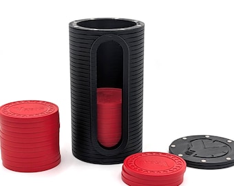 Op de afbeelding: Een zwarte cilindervormige opbergcontainer met een verticaal uitgesneden venster, gevuld met rode ronde spelchips. Een stapel rode chips staat links, een kleinere stapel rechts en een zwart rond deksel met een logo ligt ernaast.