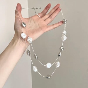 May include: A double-strand necklace featuring alternating polished silver-tone metallic beads and irregular white beads. The necklace is constructed with thin silver-tone chains and includes a lobster claw clasp closure at the back of the neck.