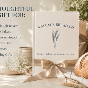 Puede incluir: Un libro de tapa dura blanco titulado Wallace Bread Co. con una ilustraci&oacute;n de espigas de trigo y el texto Recipes, Baking Notes, Family Favorites. El libro est&aacute; envuelto con un lazo de sat&eacute;n beige, junto a un pan y regalos.
