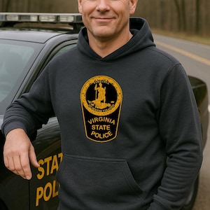 May include: Dark gray Virginia State Police hoodie with a large emblem on the front. The emblem is a gold and black design with the words "Virginia State Police" and a silhouette of a person. The hoodie has a front pocket.