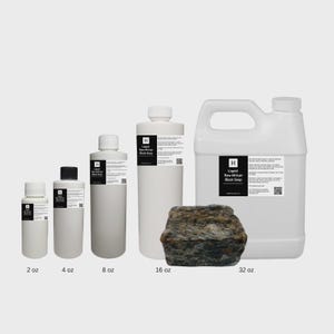 May include: Various sizes of Liquid Raw African Black Soap are displayed, ranging from 2 oz to 32 oz. The containers are white with black labels. A rough, dark brown chunk of raw black soap is also present.