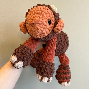 May include: A brown and orange crocheted plush toy with a long snout and four legs. The toy has a white crocheted nose and white crocheted feet.
