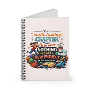 Op de afbeelding: Een wit spiraalgebonden notitieboek met een kleurrijke omslag. De omslag toont de tekst "I'm a multi-tasking CRAFTER. I can trip over NOTHING and start a NEW PROJECT at the same time." met illustraties van ambachten.