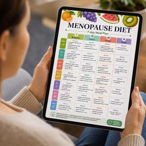 Peut inclure: Une tablette affiche un plan de repas de 7 jours intitulé "MENOPAUSE DIET". Le plan est divisé en sections petit-déjeuner, déjeuner, dîner et collation, avec une variété d'options alimentaires répertoriées pour chaque jour. Des icônes colorées et des illustrations de fruits et légumes sont en haut.