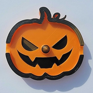 May include: Orange and black Halloween-themed pumpkin-shaped ashtray. The ashtray features a carved jack-o'-lantern face with a brown nose. The rim and face details are black, while the pumpkin body is orange.