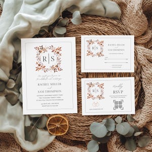 May include: A collection of wedding stationery with a floral wreath design and the initials "RS". The invitation, RSVP, and details cards are on white paper with elegant typography. The color scheme includes brown, beige, and orange accents.