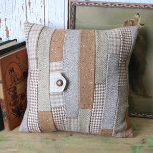 Può includere: Un cuscino patchwork marrone, beige e bianco con un solo bottone marrone. Il cuscino è realizzato con diversi tessuti con un motivo a spina di pesce, a quadri e a pied-de-poule.