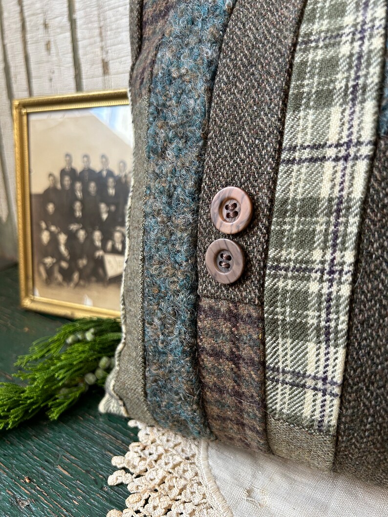 K&ouml;nnte beinhalten: Ein braunes und gr&uuml;nes Patchwork-Kissen mit zwei braunen Kn&ouml;pfen. Das Kissen ist aus verschiedenen Stoffen gefertigt, darunter karierter Stoff und Tweed.